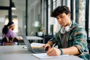 Student taking notes and working at a laptop